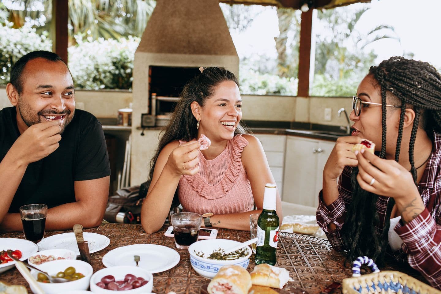 Three friends laughing together over a meal on a sunny terrace